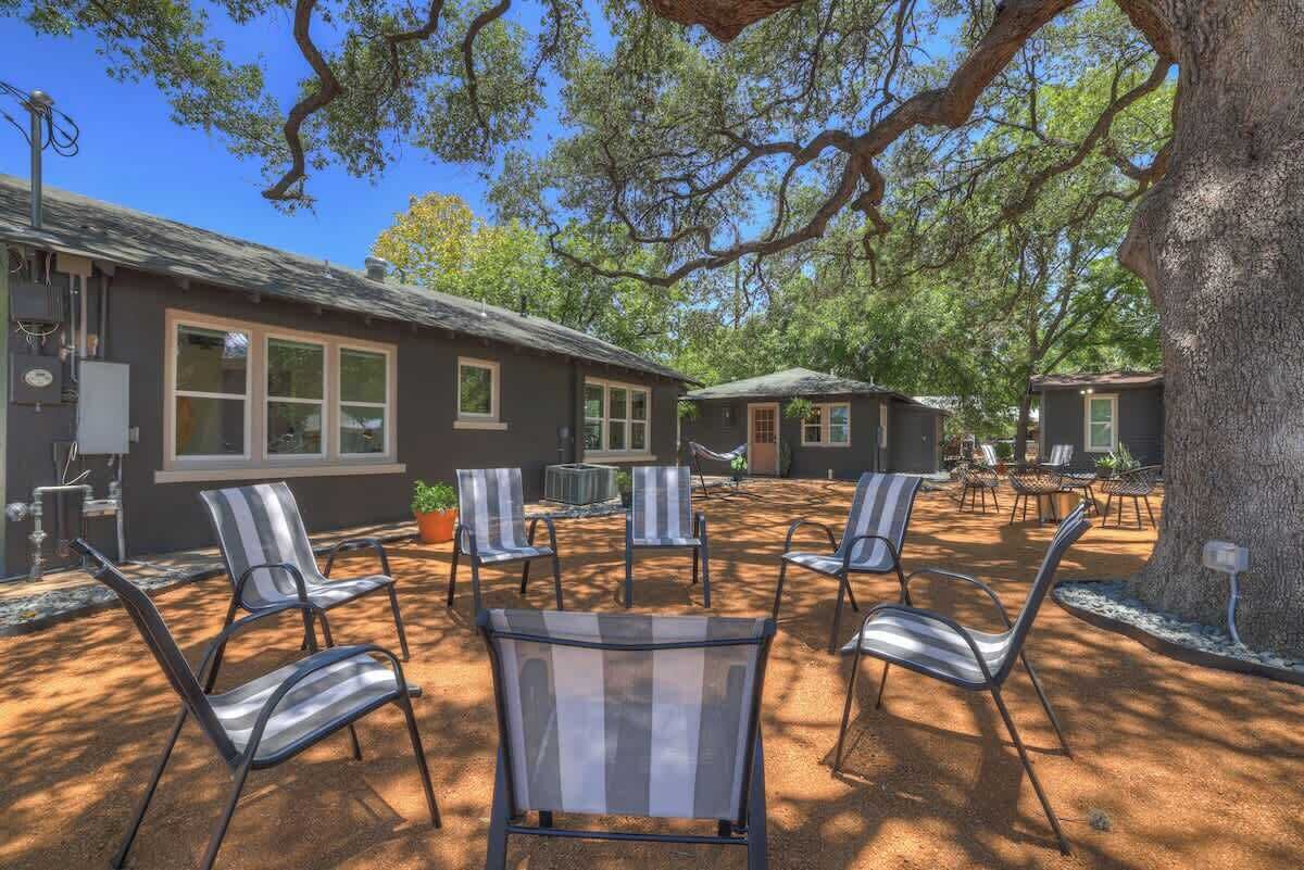 Un espace patio avec des sièges d’extérieur, un bâtiment doté de grandes fenêtres et un arbre qui offre de l’ombre.