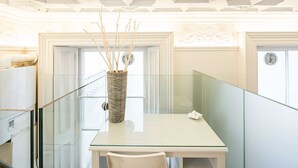 Une pièce moderne avec un bureau en verre, une chaise blanche et un vase décoratif orné de branches.