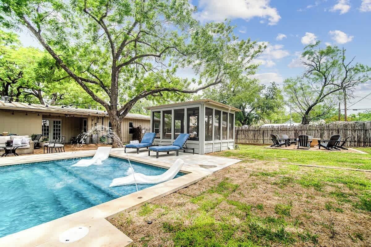 A backyard with a swimming pool, a covered patio area, and outdoor furniture.