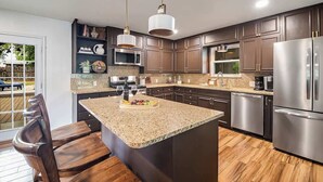 Een moderne keuken met donkere kastjes, granieten werkbladen, roestvrijstalen apparatuur en een centraal eiland met zitplaatsen.