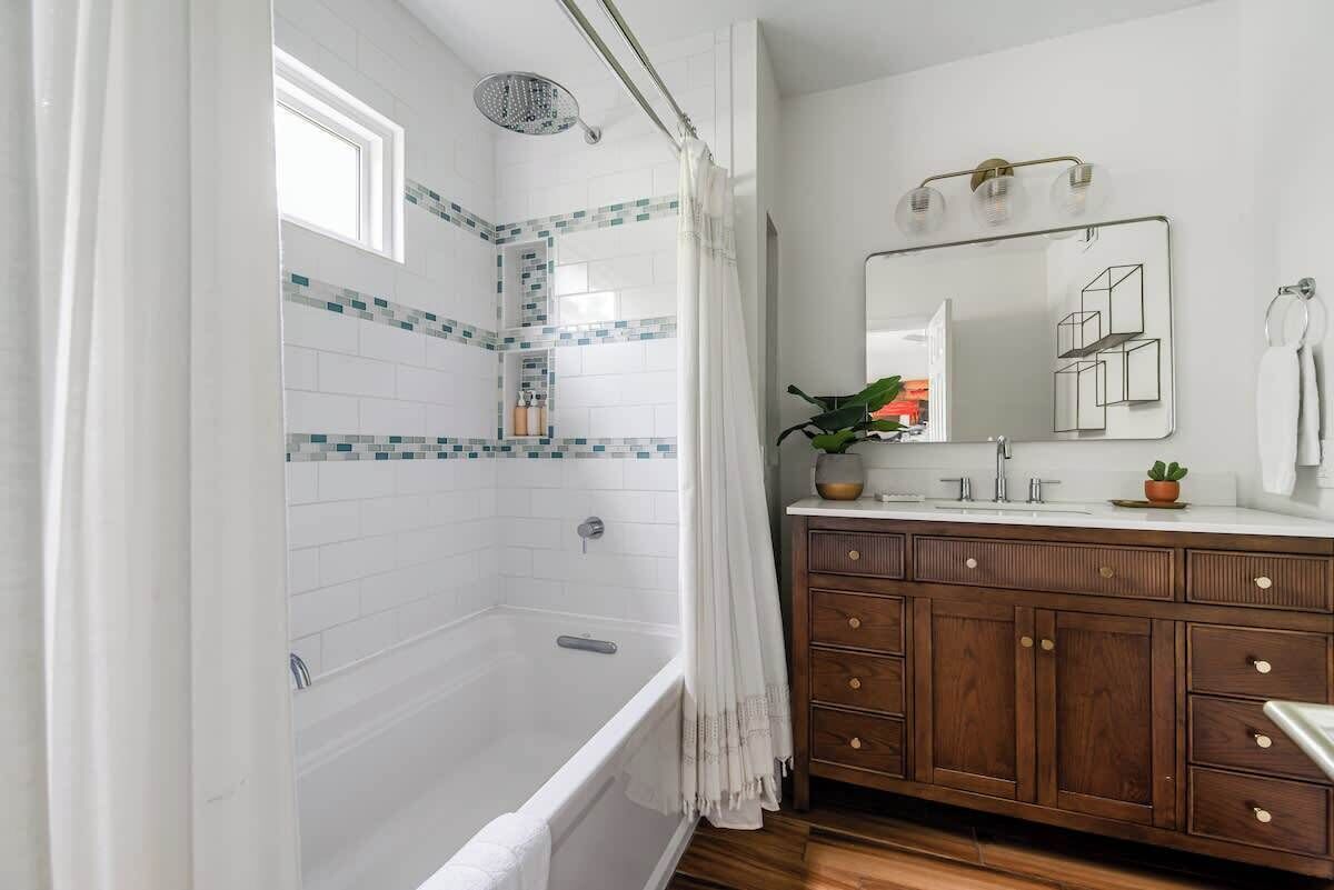 Un bagno con vasca, doccia, mobile lavabo con specchio e finestra.