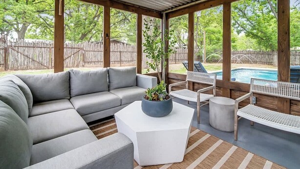Een overdekt terras met een grijze modulaire bank, een witte salontafel en een kleine ronde tafel. Er is een zwembad in de achtergrond te zien.