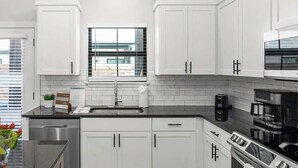 Una cucina moderna con mobili bianchi, un lavello in acciaio inossidabile, una finestra con persiane e un forno integrato.