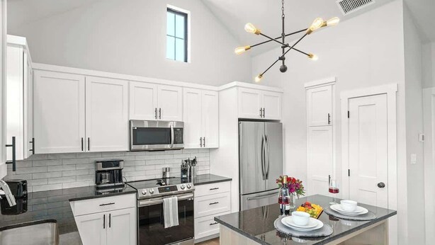 Una cucina moderna con mobili bianchi, elettrodomestici in acciaio inossidabile, un'isola centrale e una lampada a sospensione.