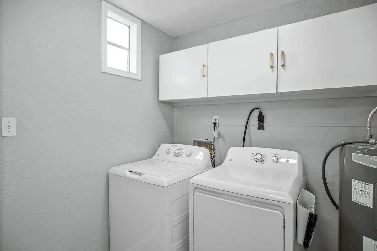 A laundry room with two white washing machines, a cabinet above, and a water heater.