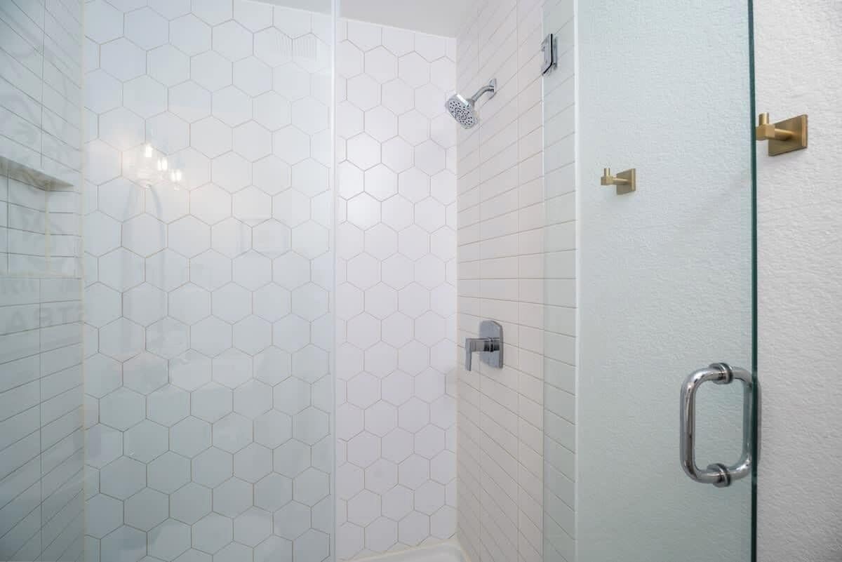 A shower with a glass door and a hexagonal tile pattern on the walls.