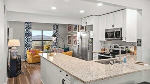A modern kitchen with white cabinets, a granite countertop, stainless steel appliances, and a view of the mountains. - Hochland Haus (Boerne)
