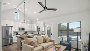 A modern kitchen with stainless steel appliances, a central island, and a dining area with a sofa and coffee table. - Lucille's Abode With Hot Tub (Fredericksburg)