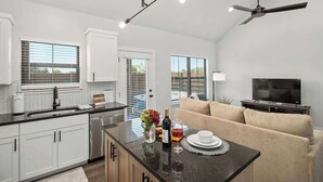 A modern kitchen with white cabinets, a black countertop, and a dining area with a beige sofa. - Lucille's Abode With Hot Tub (Fredericksburg)