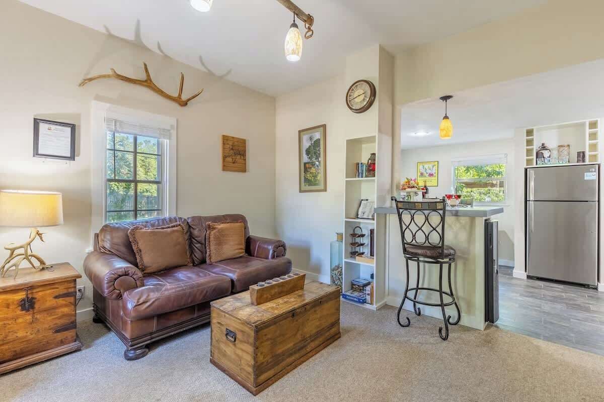 A cozy living room with a brown leather sofa, a wooden chest, and a dining area with a bar.