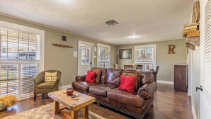 A living room with a brown leather sofa, a wooden coffee table, and a green armchair. - Two Unit Oasis With Two Hot Tubs (Fredericksburg)