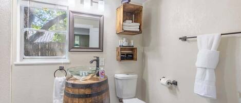 A bathroom with a wooden barrel sink, a toilet, a window, and a towel rack.