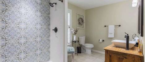 A bathroom with patterned tiles, a wooden vanity, a white sink, and a toilet.