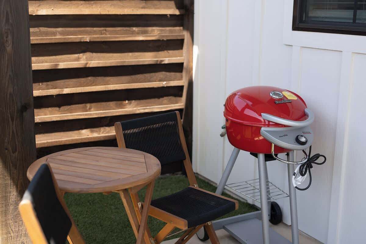 Una parrilla con panel de control, una mesa de madera y dos sillas en un patio trasero.