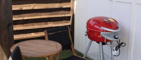 Una parrilla con panel de control, una mesa de madera y dos sillas en un patio trasero.