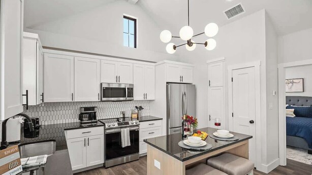 A modern kitchen with white cabinets, a central island, stainless steel appliances, and a dining area with a blue upholstered sofa. - Fred's Joint With Hot Tub (Fredericksburg)