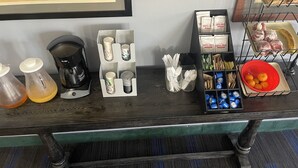 A kitchen counter with various items including a coffee maker, condiment bottles, utensils, and food items. - Hotel Yuma (Yuma)