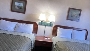 A hotel room with two beds, each with a wooden headboard, white pillows, and a quilted bedspread. There are two wall-mounted lamps between the beds, and a small wooden nightstand with a lamp and a phone. - Hotel Yuma (Yuma)
