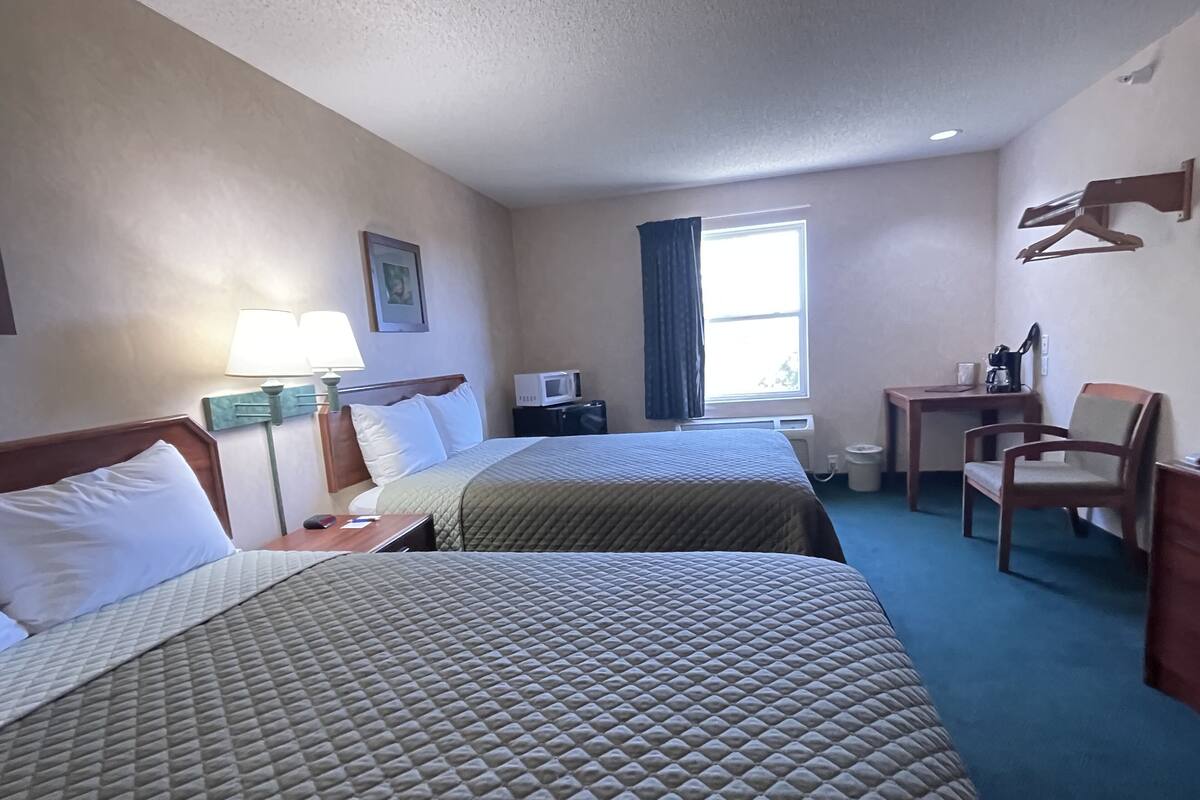 Ett hotellrum med två sängar, ett skrivbord, en stol, en mikrovågsugn och ett fönster med gardiner.