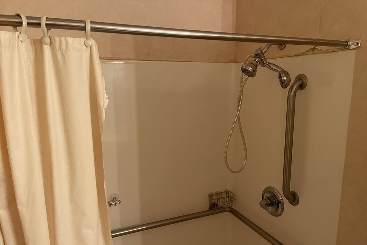 En duschhörna med ett stödhandtag, ett duschmunstycke som kan hållas i handen och en handdukshängare.
