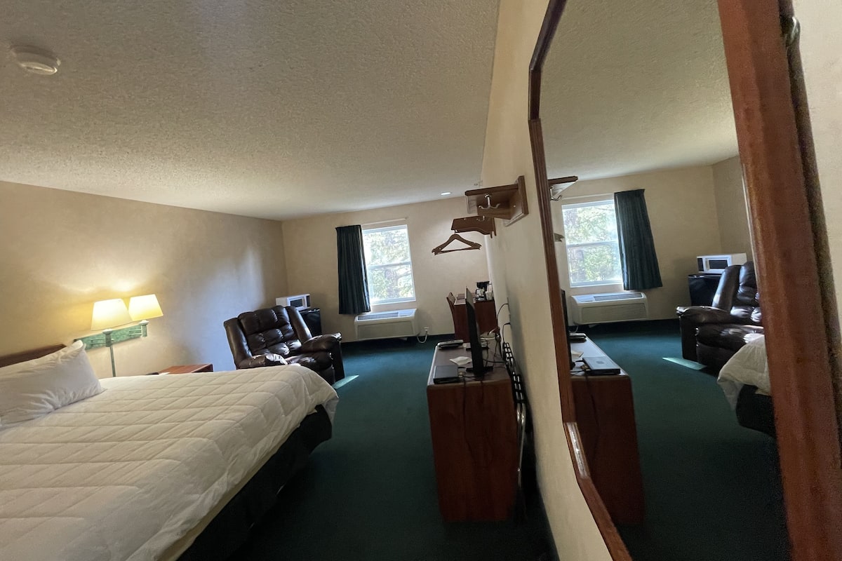 Ett hotellrum med två sängar, ett skrivbord, en stol, en spegel och ett fönster.
