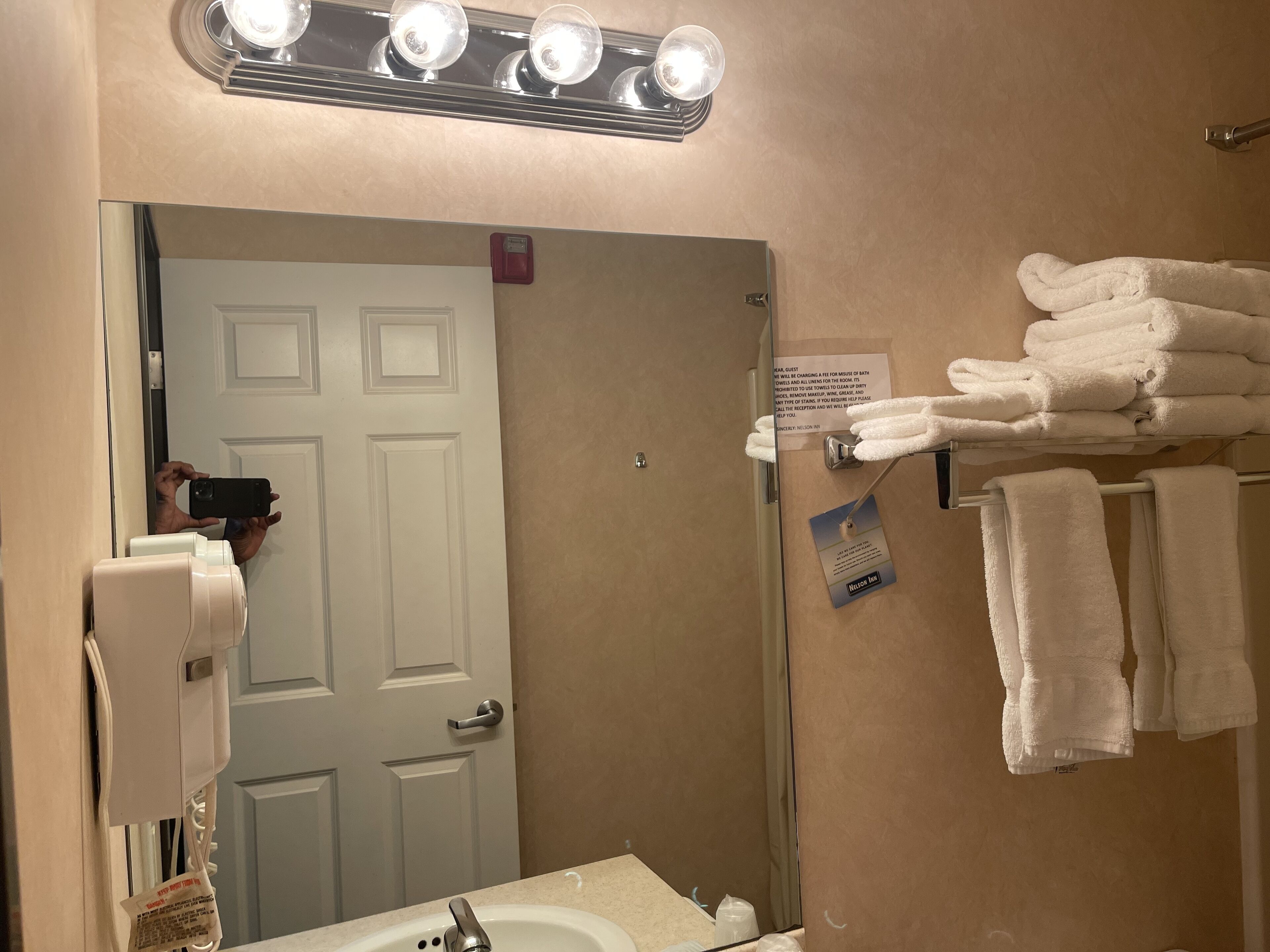A bathroom with a sink, mirror, towel rack, and a sign with a message.