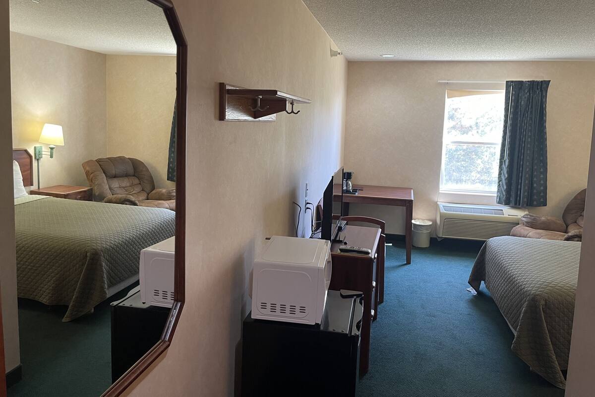 Ett hotellrum med två sängar, ett skrivbord, en stol, en spegel, en lampa och ett fönster med gardiner.