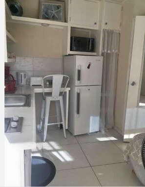 A compact kitchen with a white refrigerator, a microwave, a sink, and a chair.