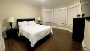 Un dormitorio con una cama, dos mesitas de noche con lámparas, un aparador y una luz en el techo.