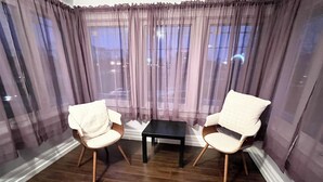 Una habitación con dos sillones blancos acolchados, una mesita negra y vistas a través de cortinas de gasa.