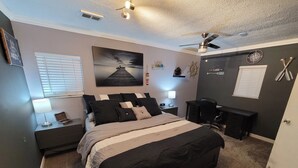 A bedroom with a bed, bedside tables, a desk, a chair, a ceiling fan, and a wall clock. - Lake St Clair Boathouse (Harrison Township)