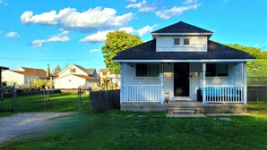 A single-story house with a porch, a small dog on the porch, and a clear sky. - Lake St Clair Boathouse (Harrison Township)