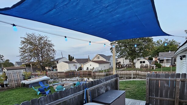 A backyard with a hot tub, wooden deck, and a blue shade sail. - Lake St Clair Boathouse (Harrison Township)
