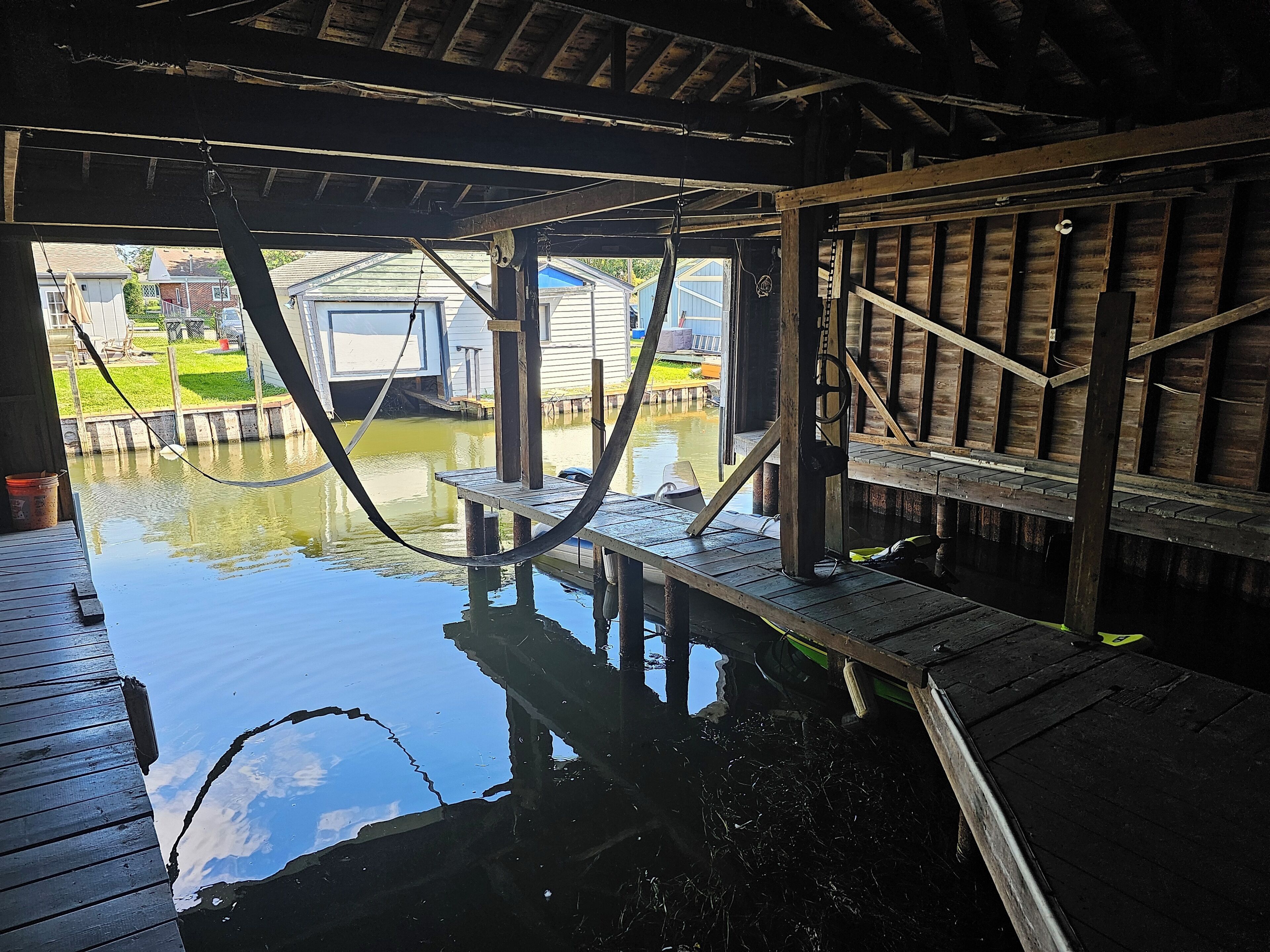 A wooden dock extending over a body of water with a clear view of a house and grassy area in the background.