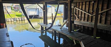 A wooden dock extending over a body of water with a clear view of a house and grassy area in the background.