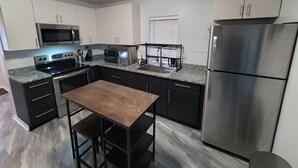 A modern kitchen with stainless steel appliances, dark cabinetry, and a wooden dining table. - Lake St Clair Boathouse (Harrison Township)