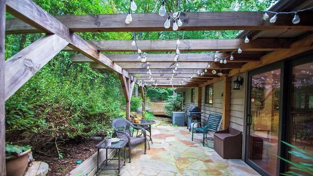 A covered patio with stone flooring, wooden pergola, and hanging light fixtures. - Murphy Mountain House - Creeks, Firepits & High Speed Internet! (Murphy)