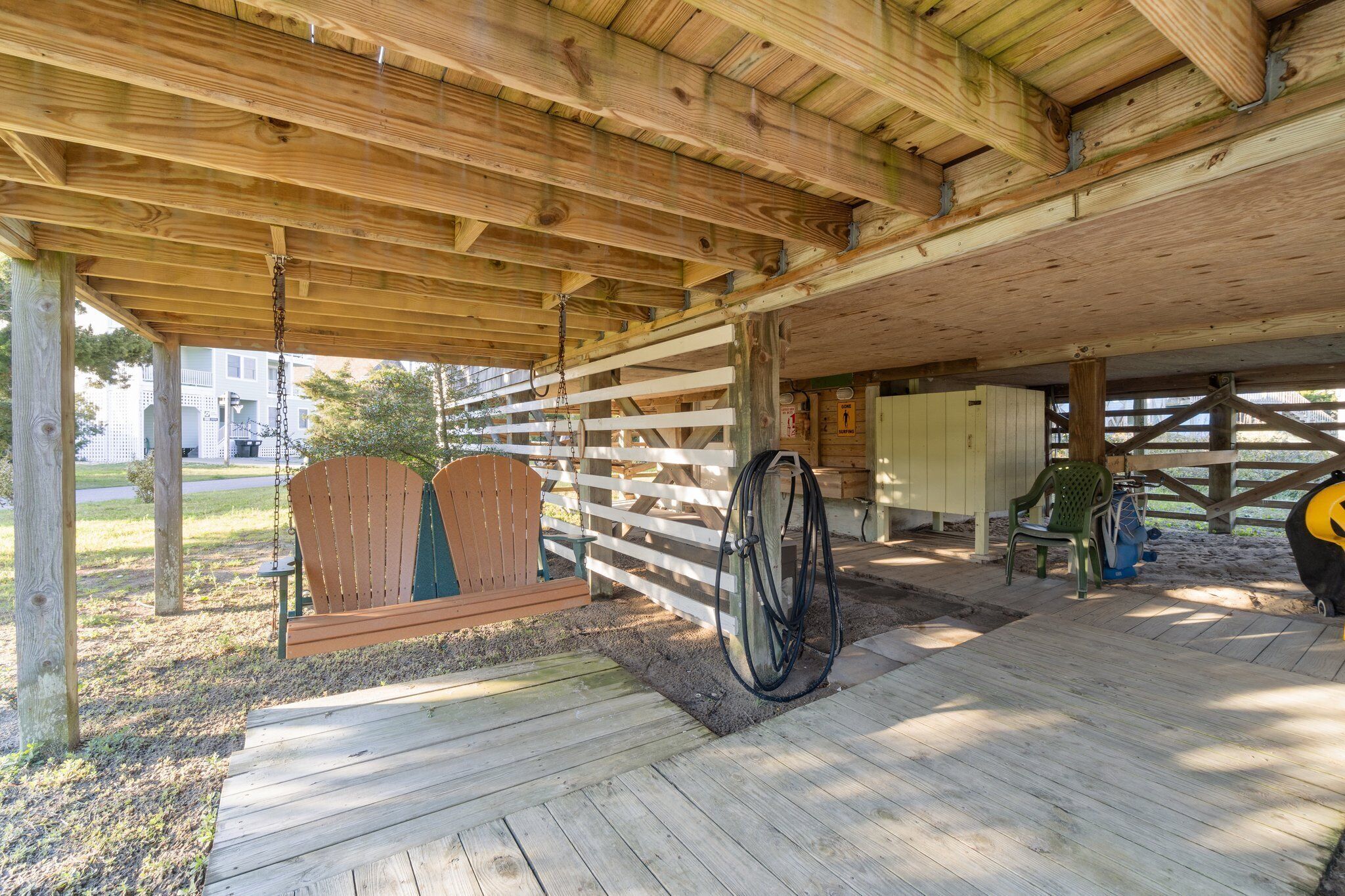 A covered wooden deck with a swing set, a bicycle, and a chair.