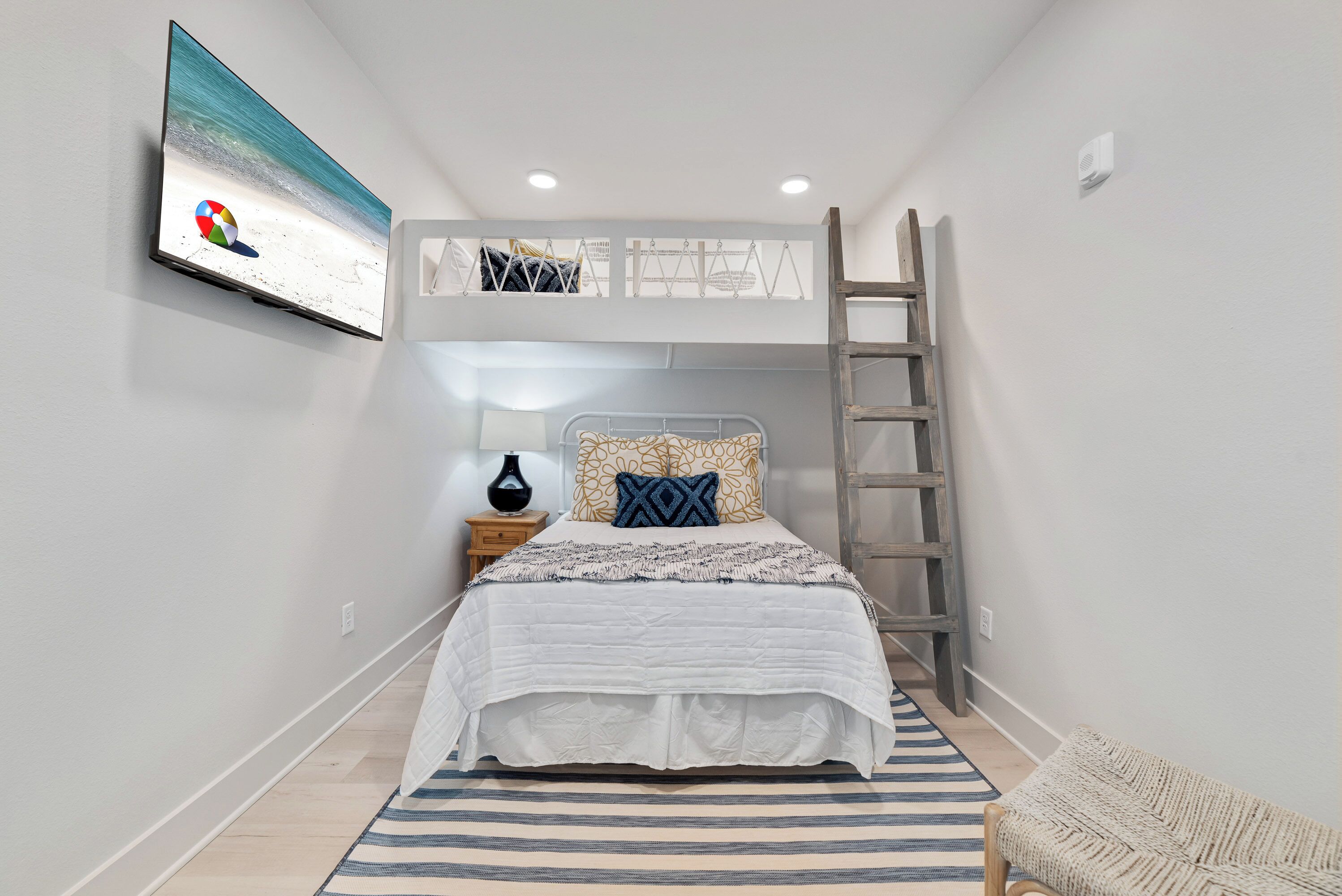 A bedroom with a bed, a TV mounted on the wall, a ladder, and a bedside table with a lamp.
