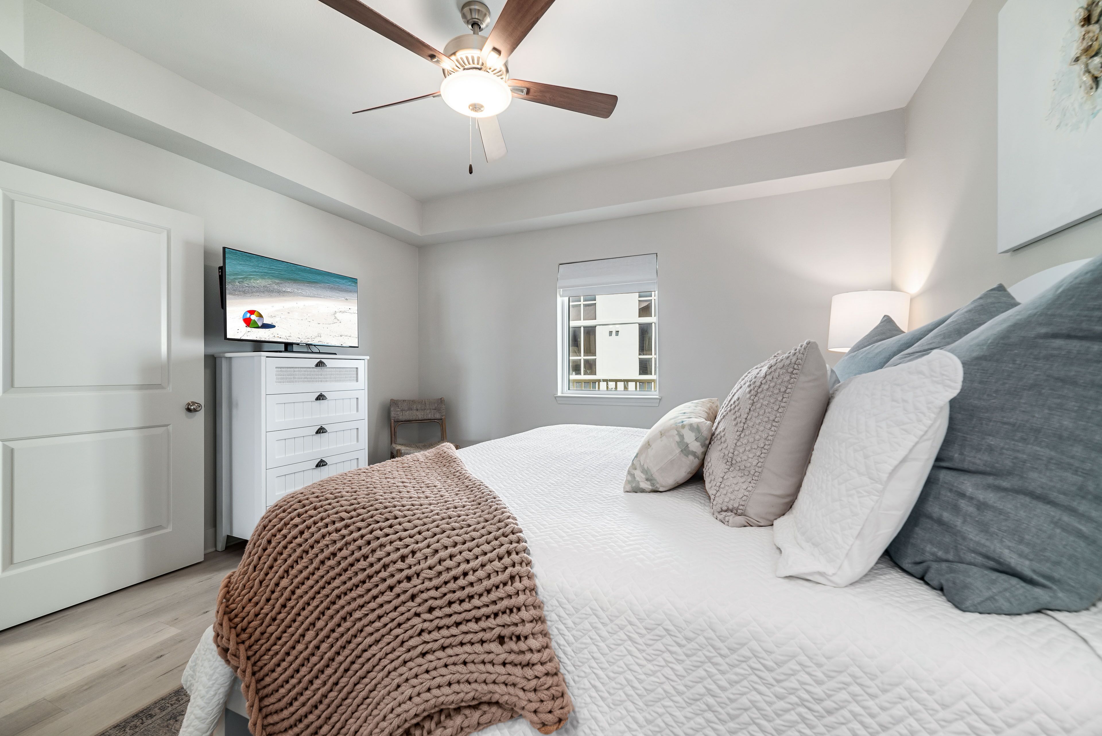 A bedroom with a bed, a ceiling fan, a TV, a dresser, and a window.
