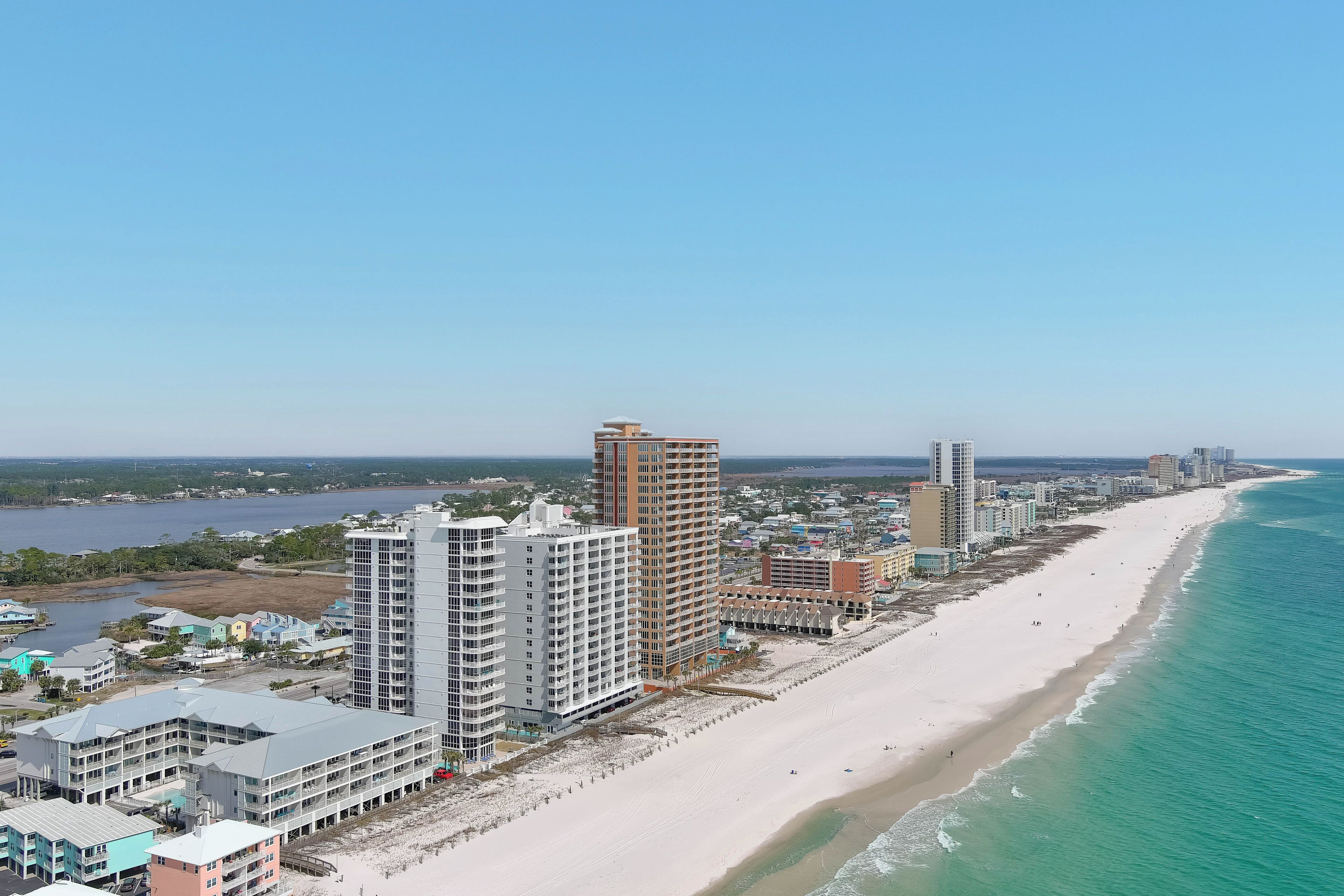 Un paysage urbain côtier avec une longue plage de sable, de hauts immeubles et un ciel bleu dégagé.