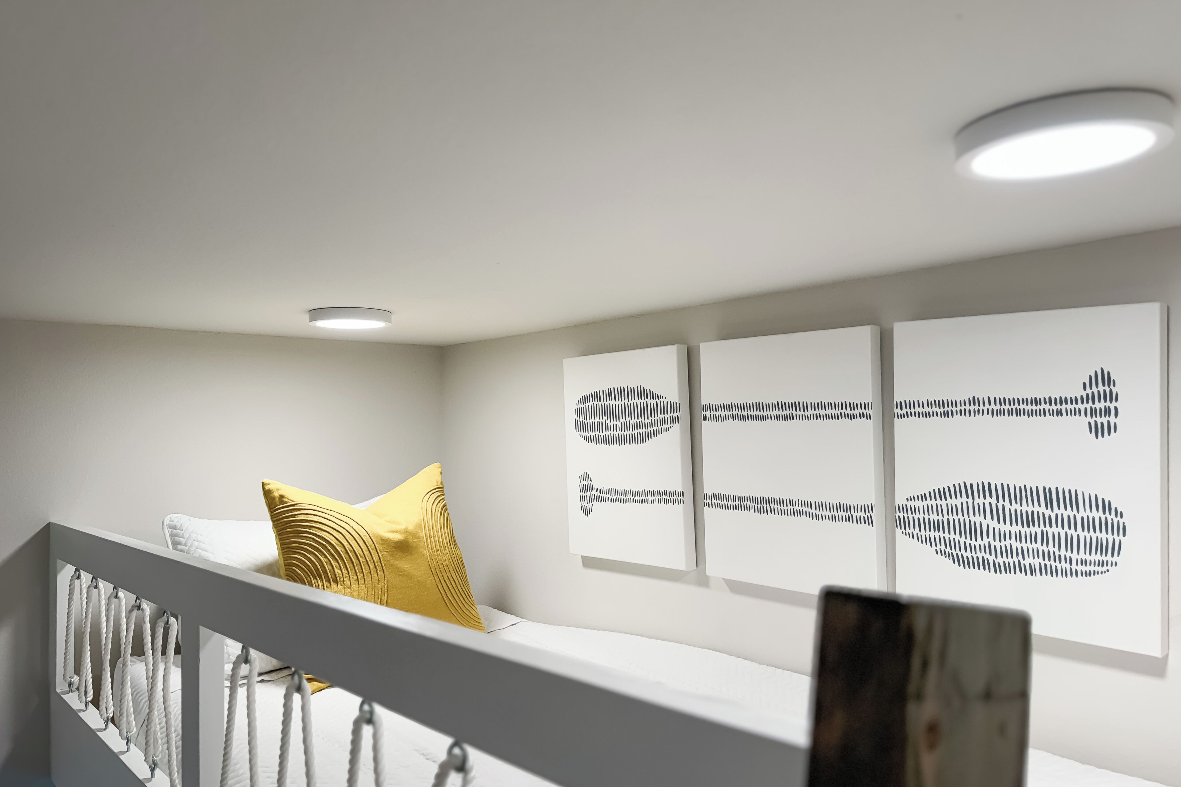 Ein modernes Interieur mit einem weißen Geländer, einem gelben Kissen und drei abstrakten Wandbildern.