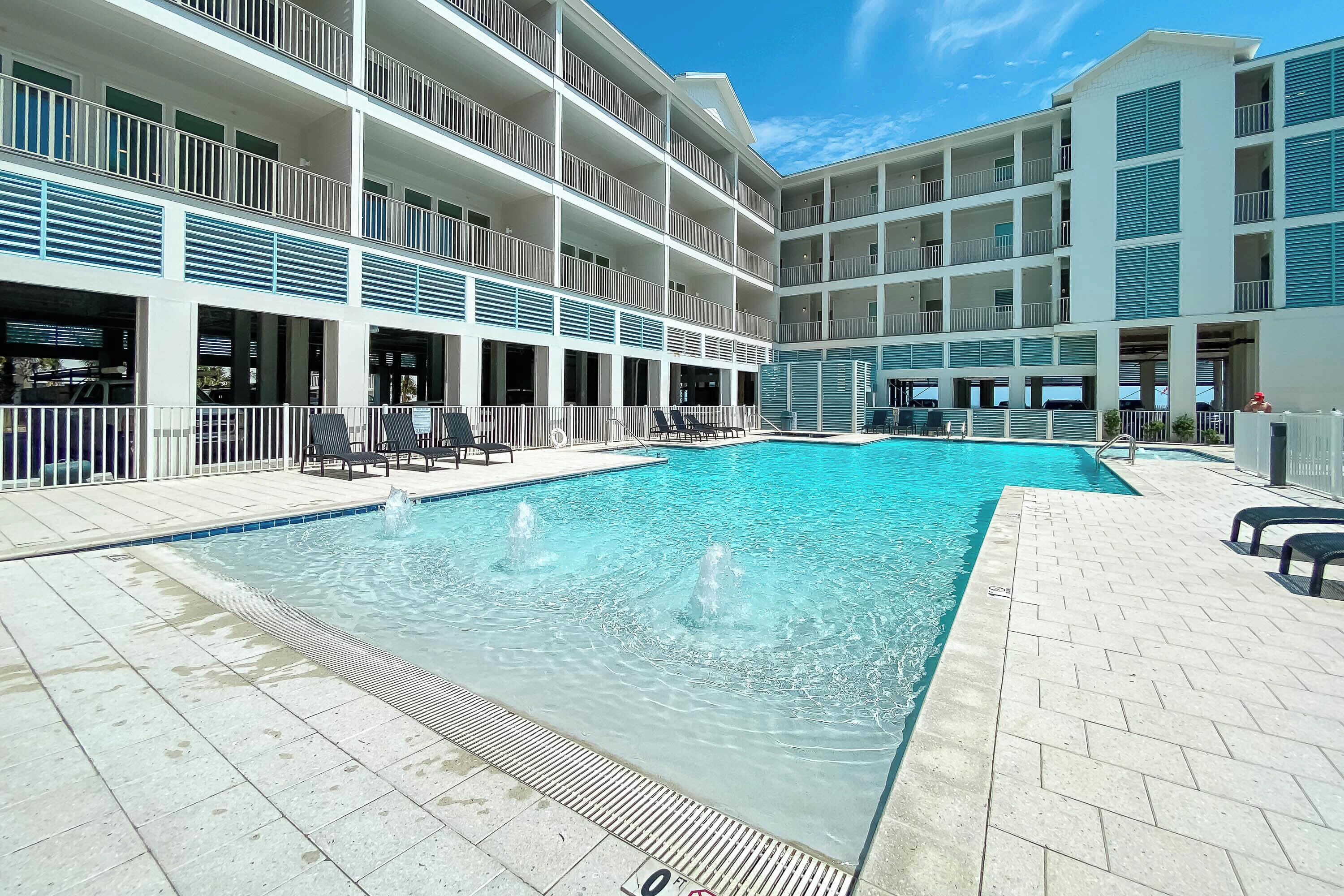 A multi-story hotel with a central swimming pool, outdoor seating, and a clear sky.
