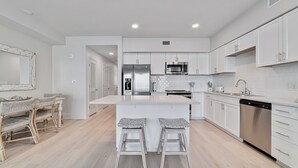 A modern kitchen with white cabinetry, stainless steel appliances, and a central island with bar stools. - "BRAND NEW" BEACHFRONT, OUTDOOR POOL, BEAUTIFUL VIEWS! (Gulf Shores)
