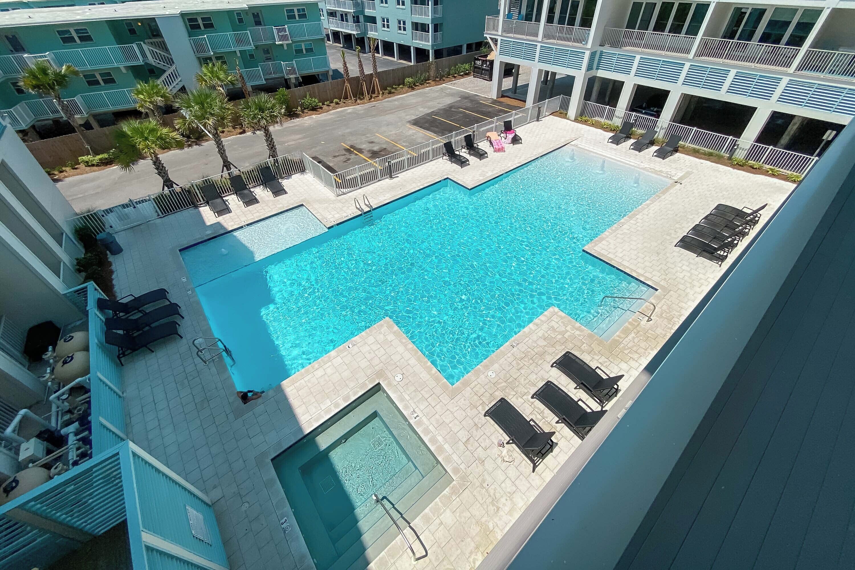 A rooftop pool with lounge chairs and a hot tub, surrounded by a multi-story building with balconies.