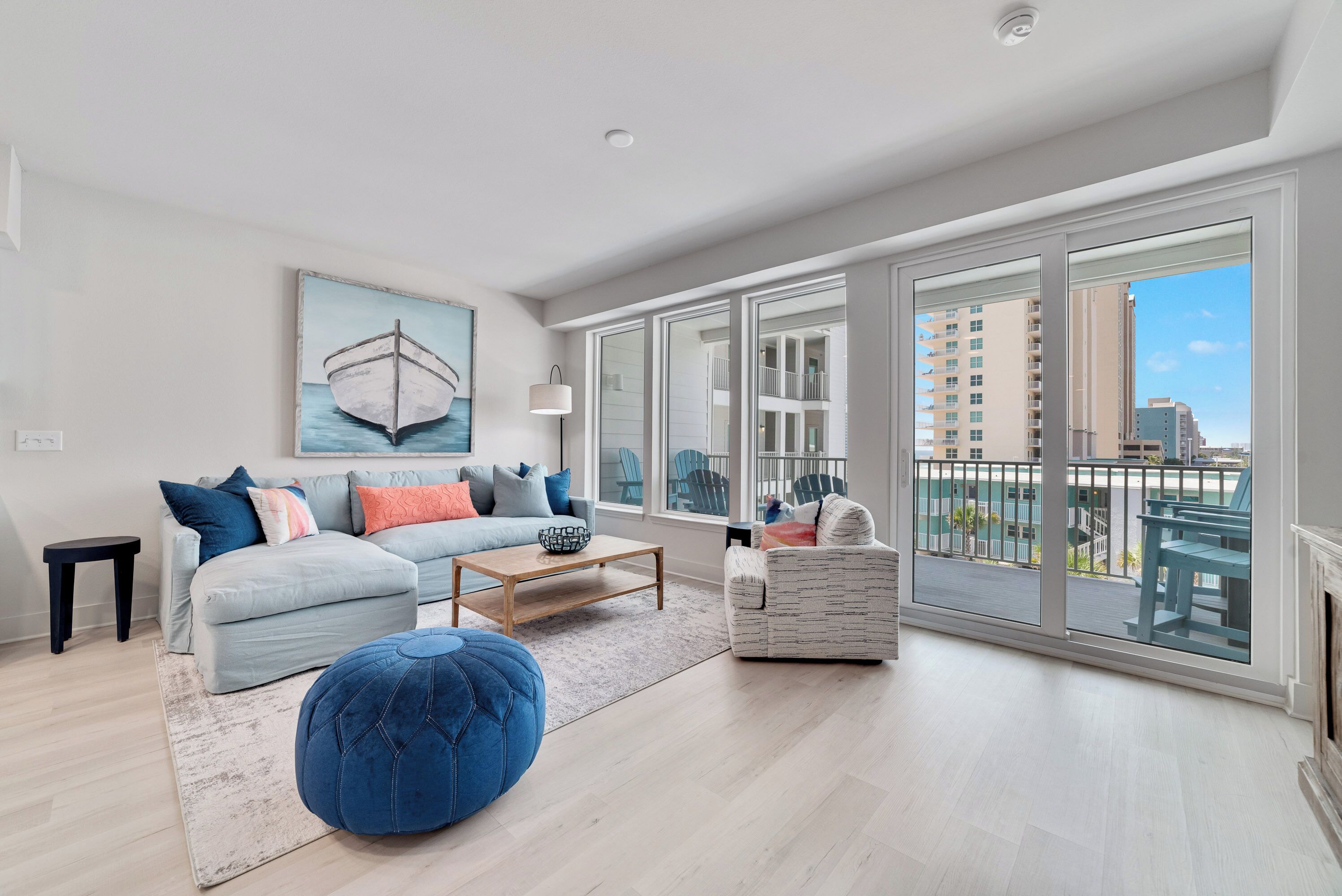 A spacious living room with a large window, a sofa, a coffee table, and a blue ottoman.