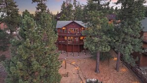 A large wooden cabin with a deck, surrounded by dense trees. - The Moose Lodge. Stunning Mtn Views. Spa. Games. (Big Bear Lake)