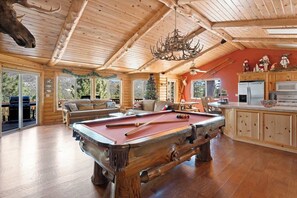 Un intérieur en bois comprenant une table de billard, un canapé et un coin cuisine.