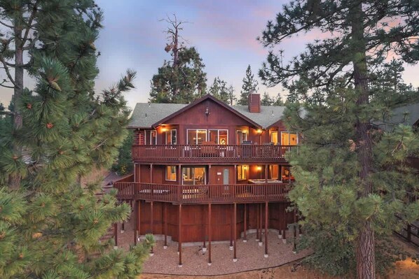 A multi-story wooden cabin with balconies, surrounded by pine trees.