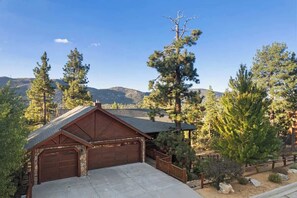 A wooden cabin with a garage, surrounded by trees and mountains.